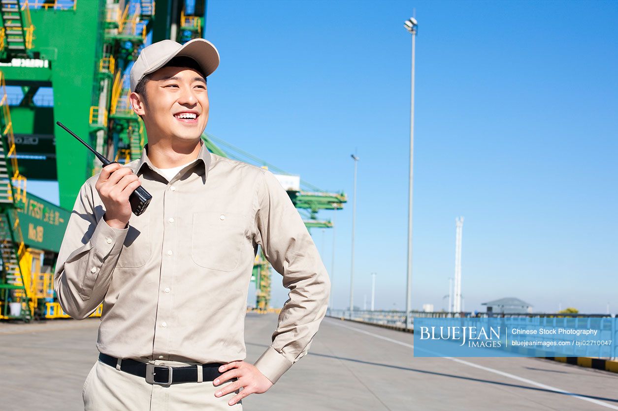 Male Chinese Shipping Industry Worker With Walkie Talkie And Crane In