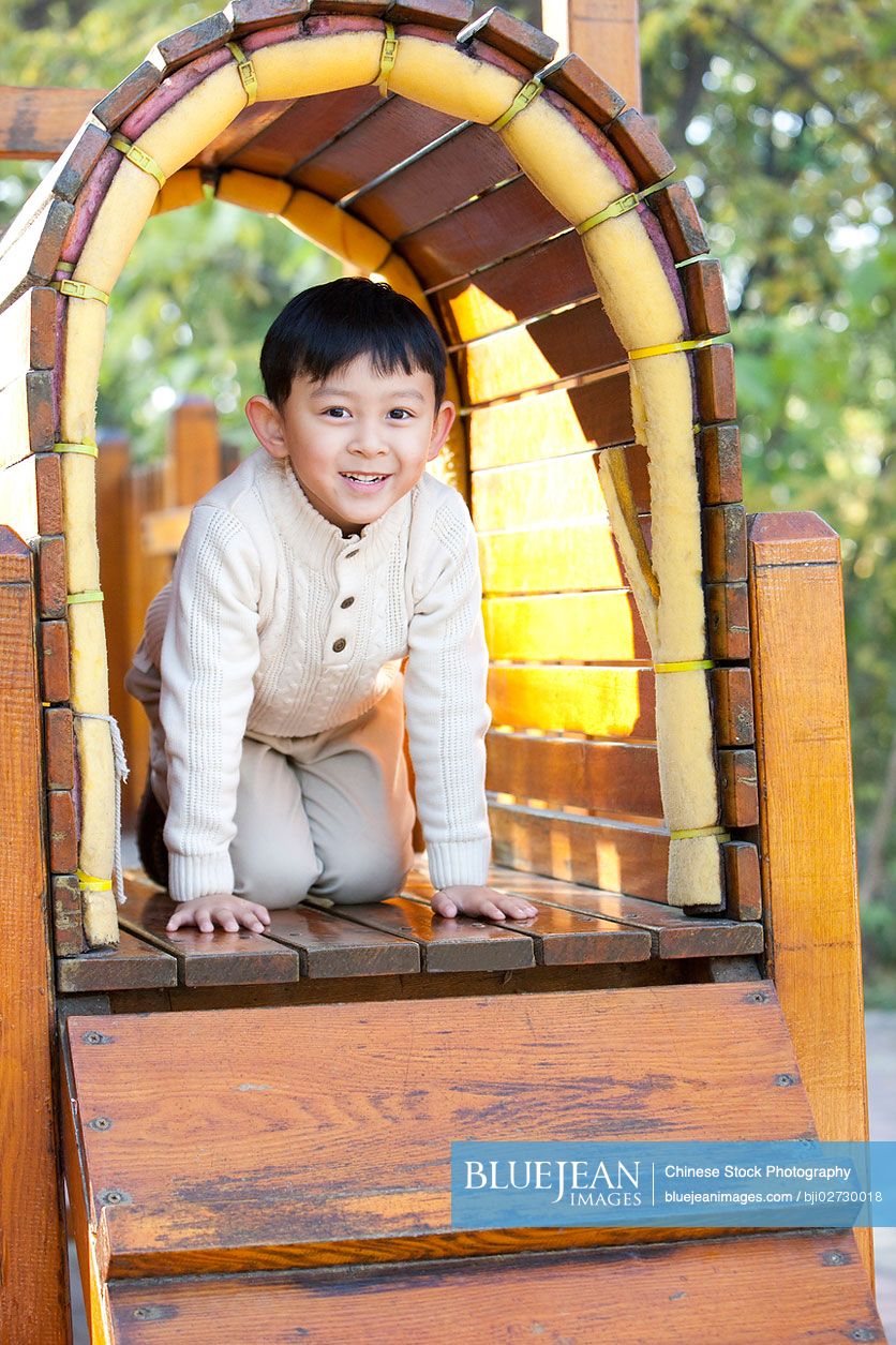 Chinese boy crawling through tunnel in playground