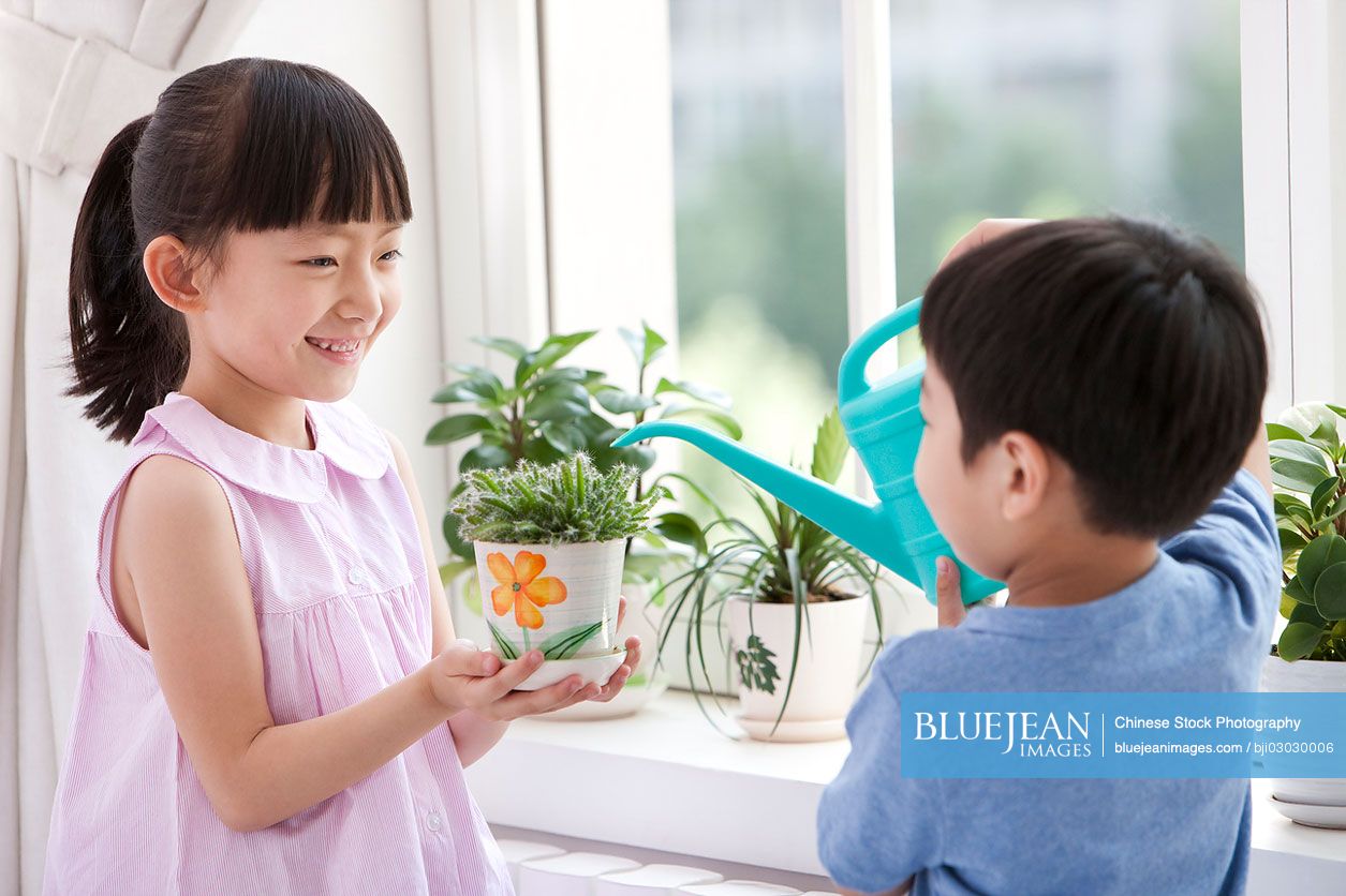 Chinese boy and girl watering potted plants together