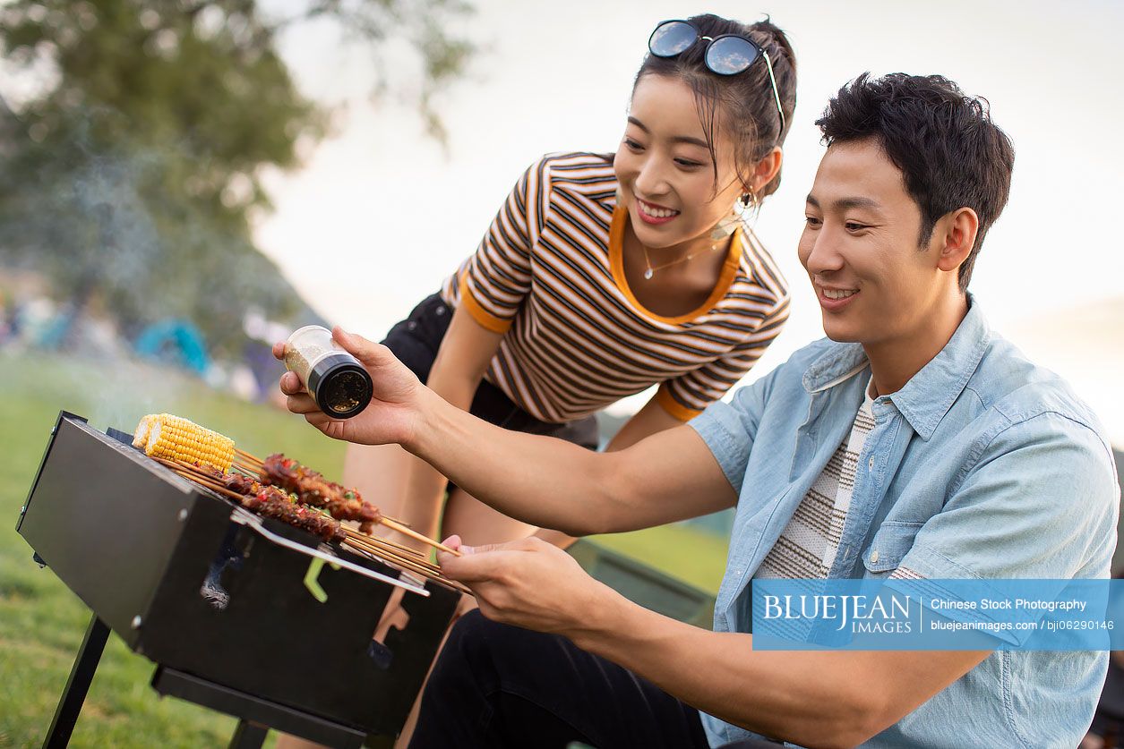 Happy young Chinese couple barbecuing outdoors