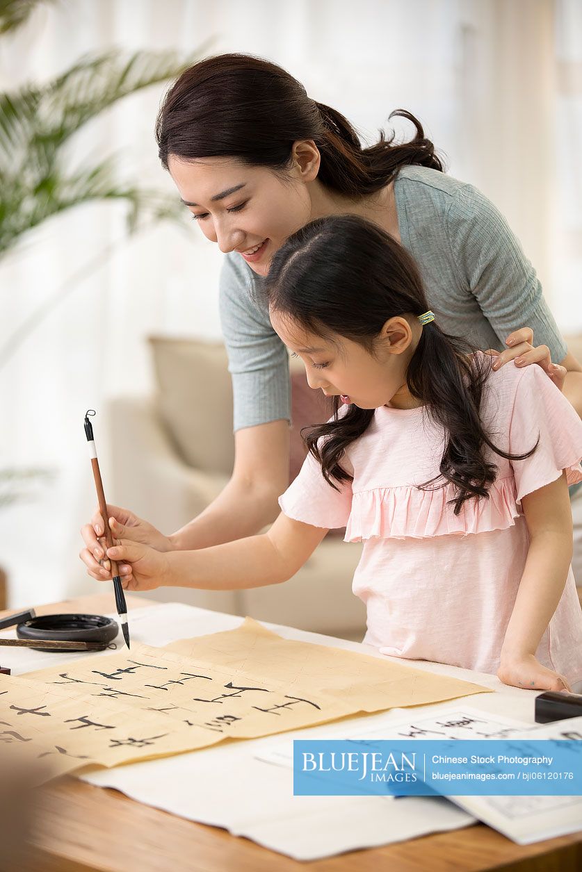 Happy Chinese mother and daughter writing calligraphy at home