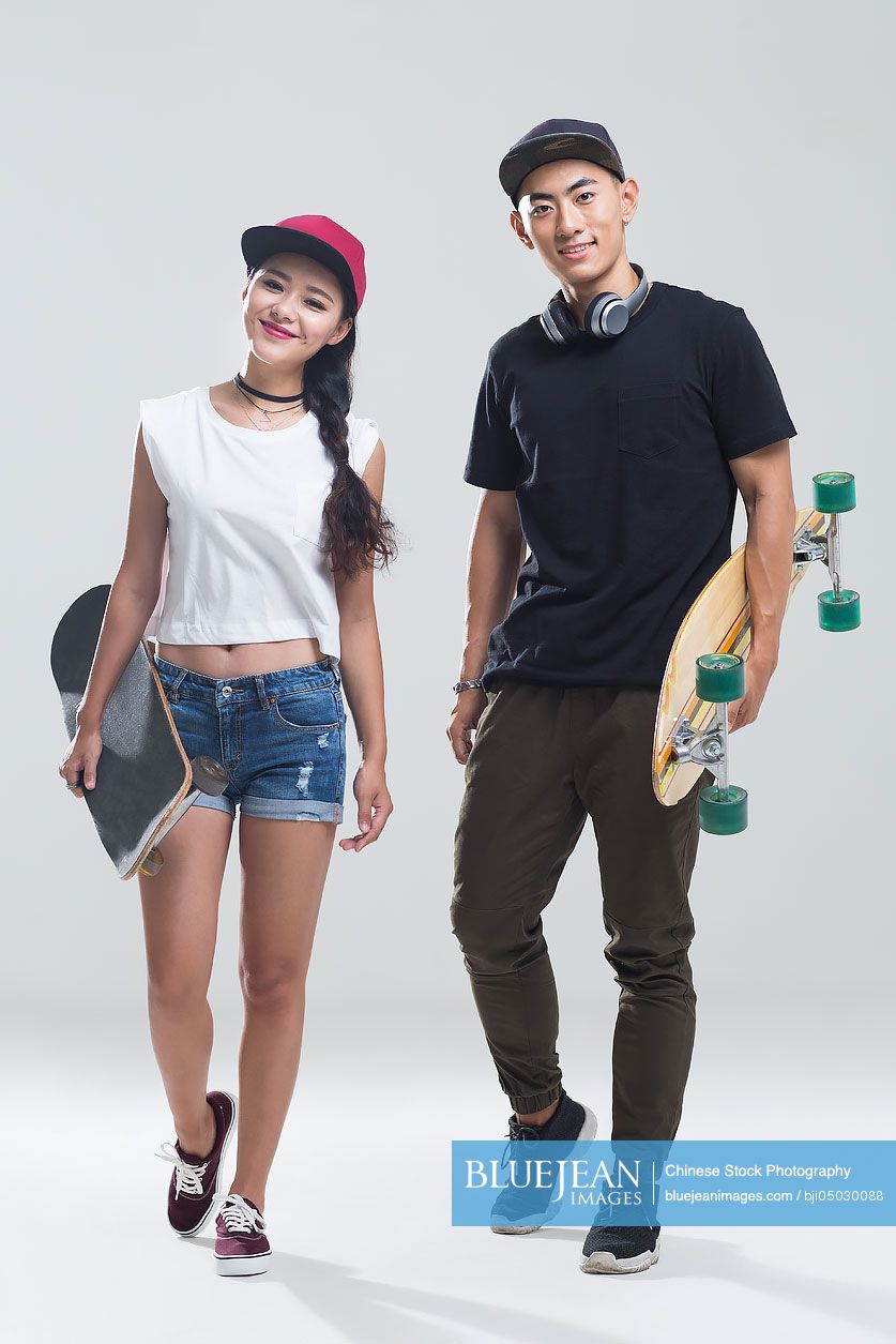 Portrait of cheerful young Chinese couple holding skateboard