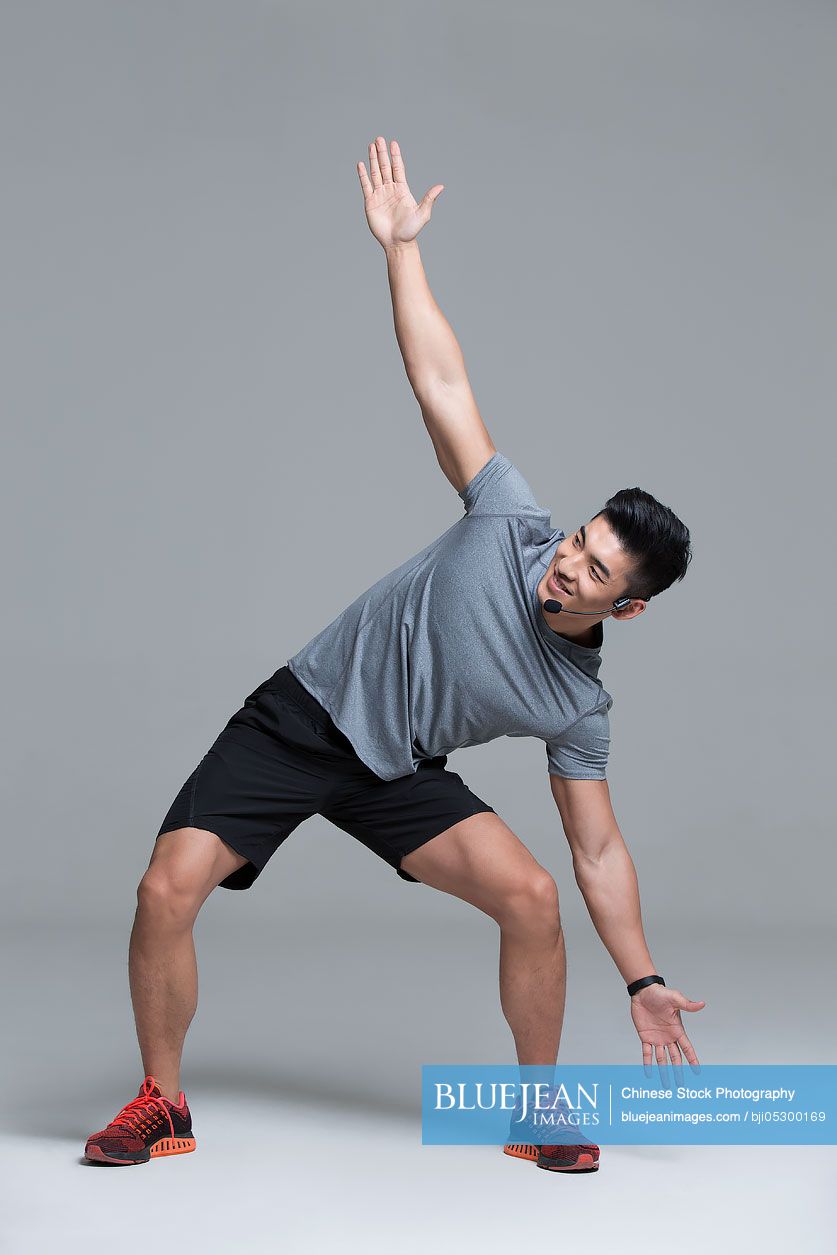 Cheerful young Chinese male trainer with headset teaching at gym