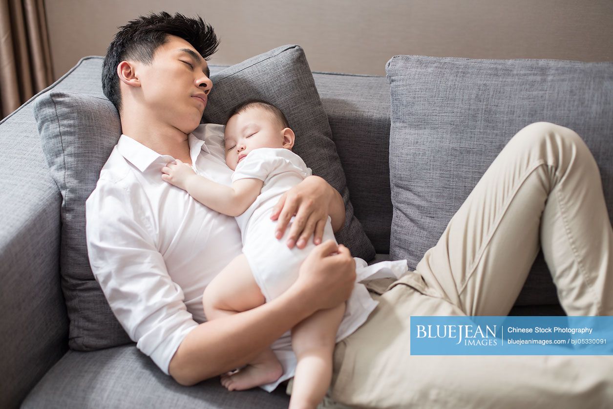 Young Chinese father and baby boy sleeping on sofa