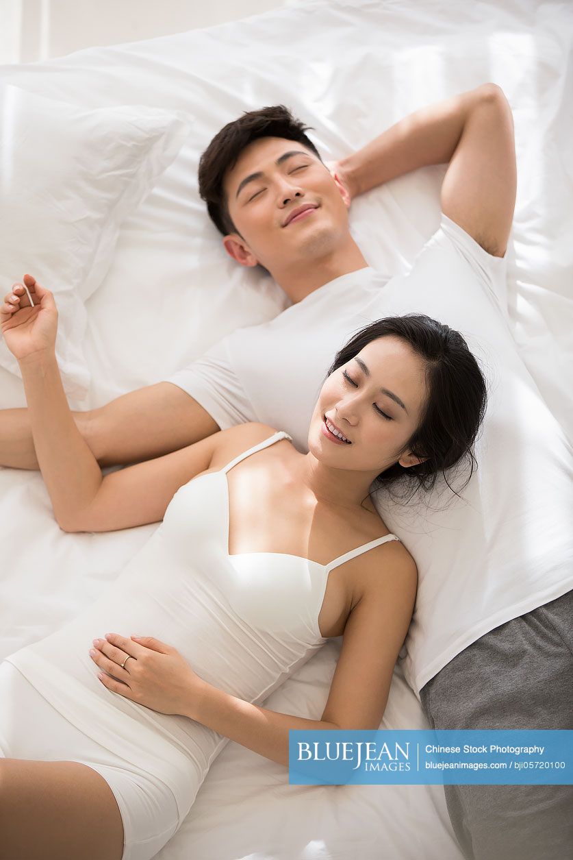 Happy young Chinese couple sleeping on bed