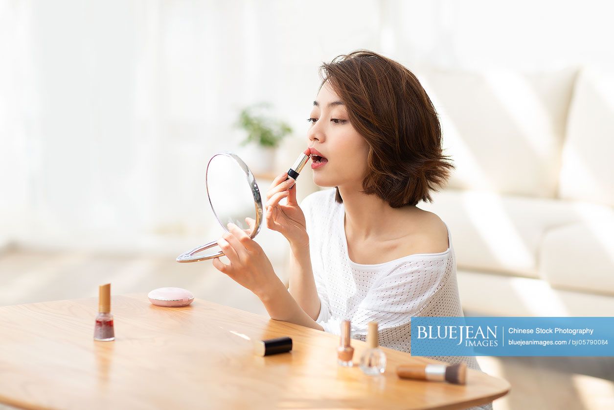 Young Chinese woman applying makeup at home