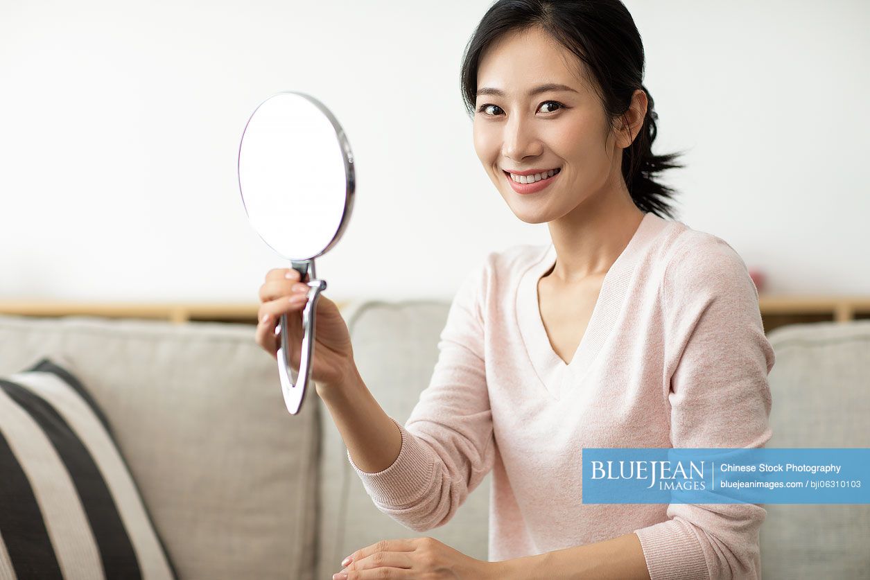 Happy young Chinese woman looking into the mirror at home