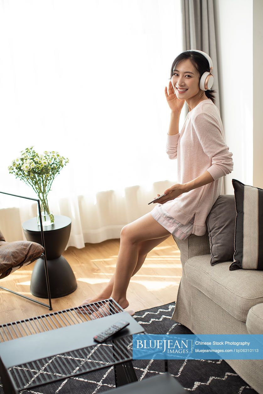 Happy young Chinese woman listening to music in living room