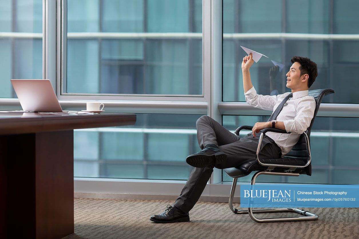 Confident Chinese businessman throwing paper plane in office