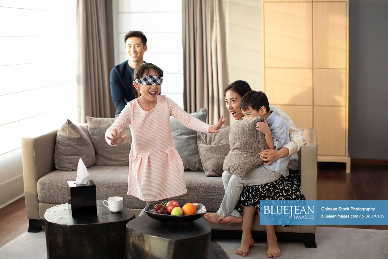 Happy young Chinese family playing hide and seek in living room