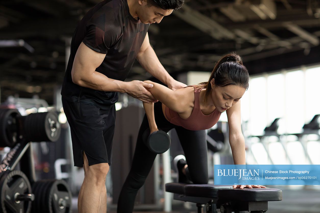 Young Chinese woman working out with personal trainer at gym