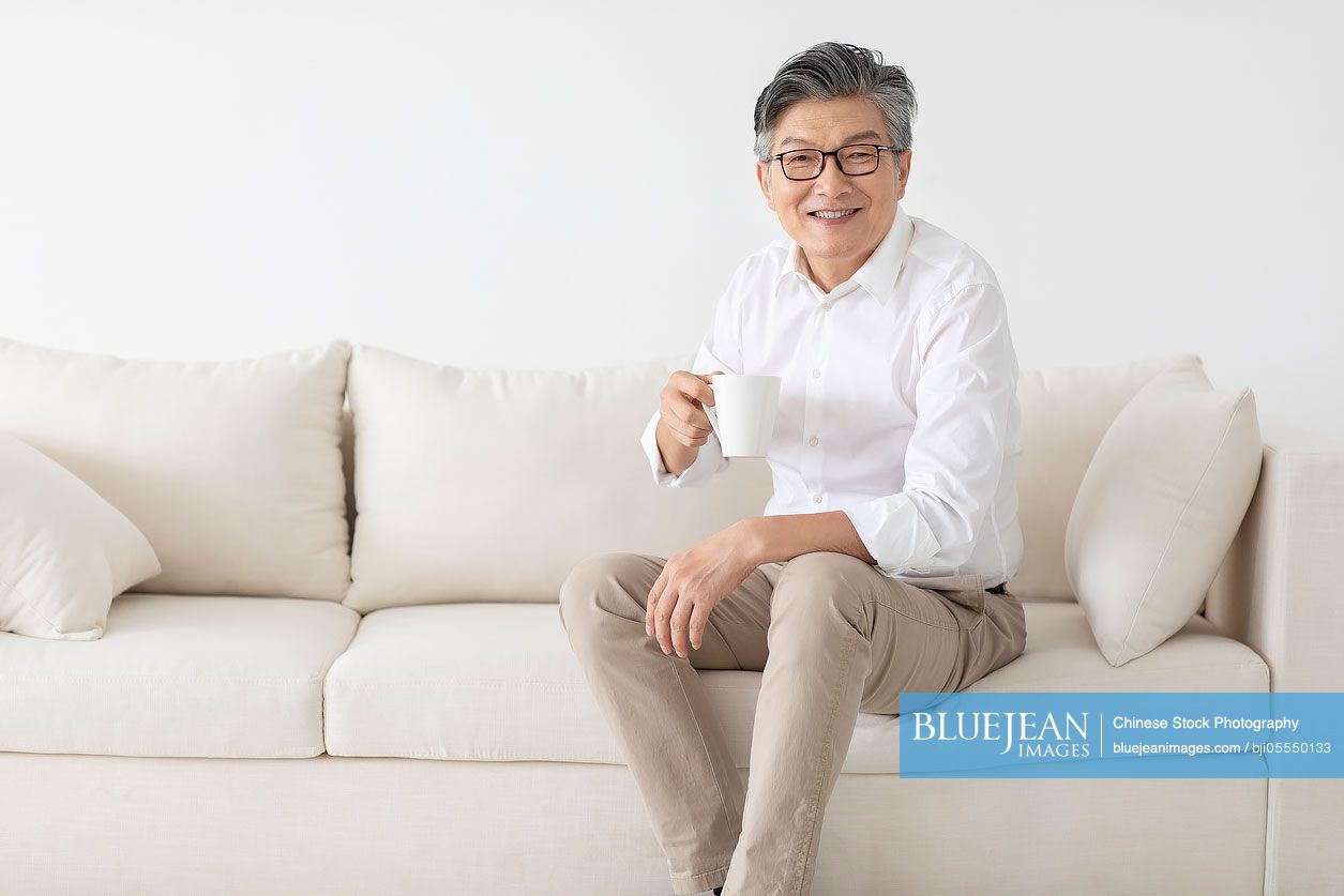 Cheerful senior Chinese man drinking coffee at home