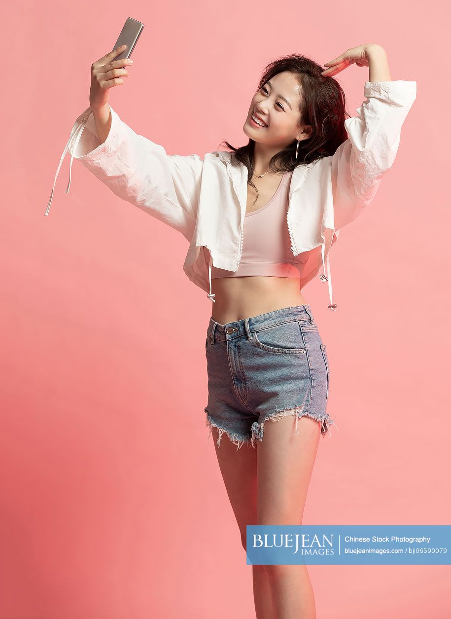 Studio shot of cute young Chinese woman using smart phone