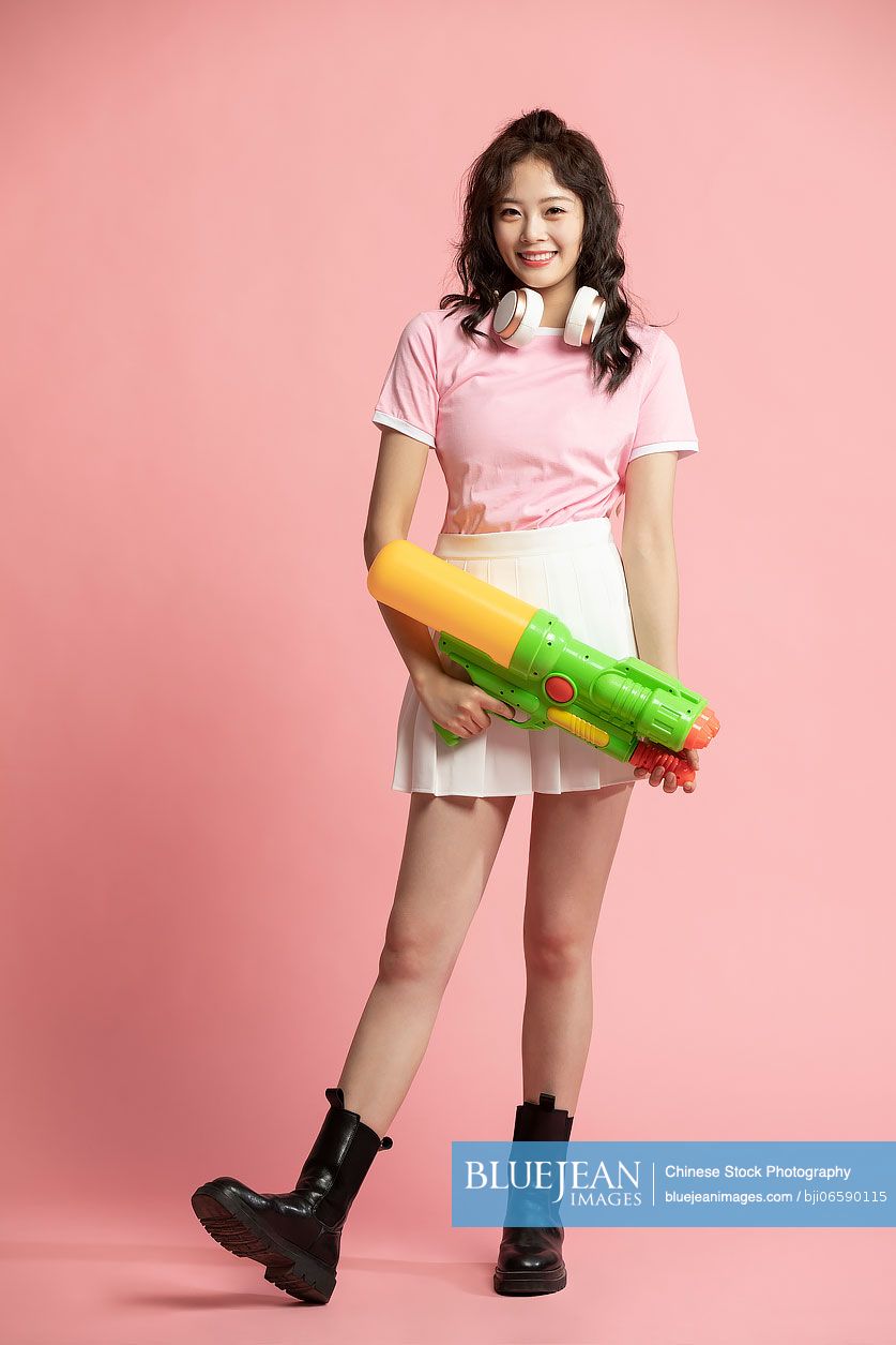 Studio shot of cute young Chinese woman holding a squirt gun