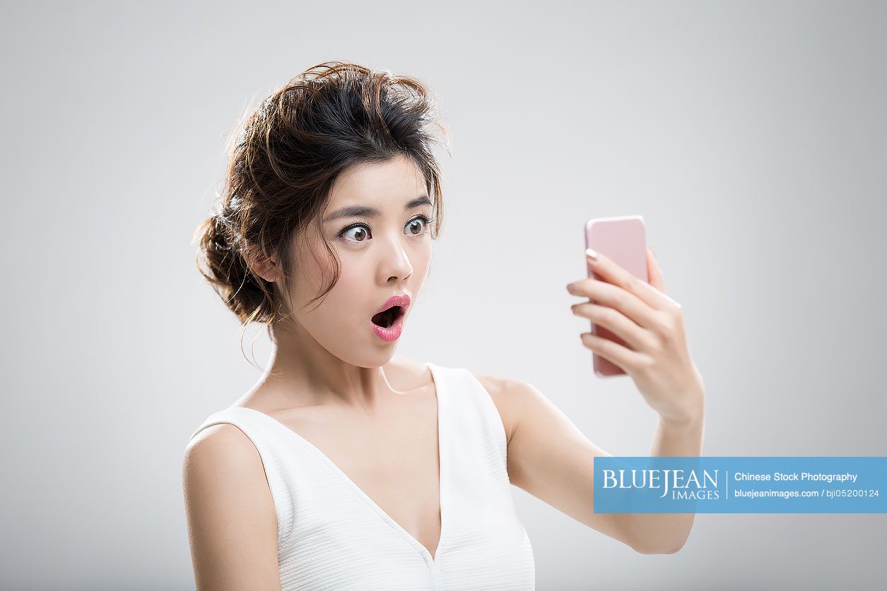 Shocked beautiful young Chinese woman looking at smart phone