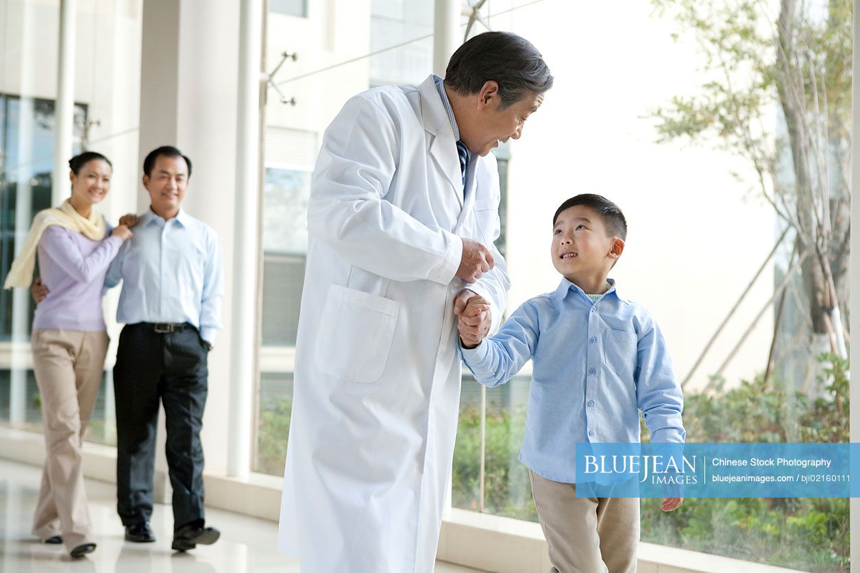 Young Chinese family walking in a hospital corridor with a doctor