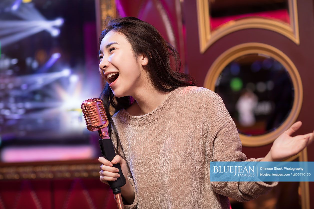 Happy young Chinese woman singing karaoke in nightclub