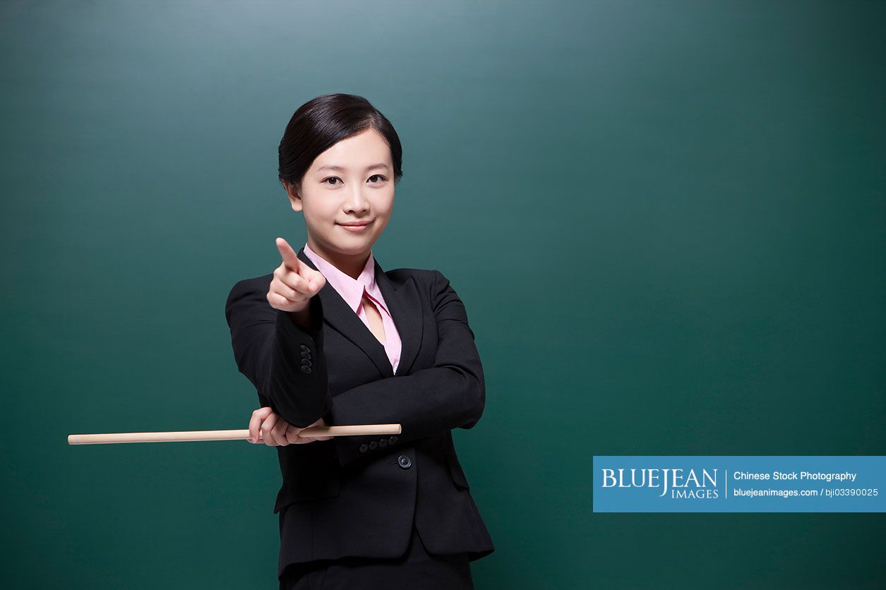 Cheerful female Chinese teacher pointing forward in classroom