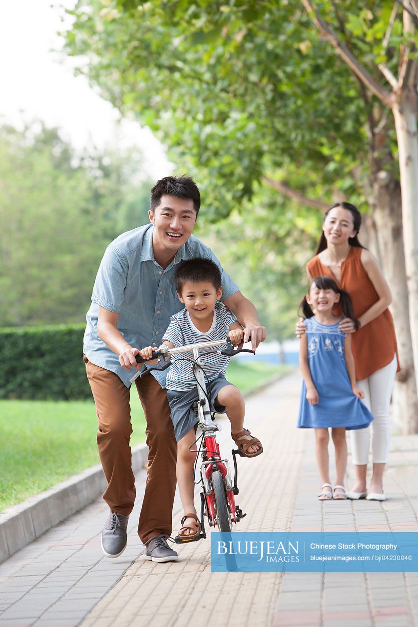 Young Chinese father teaching his son to ride a bicycle