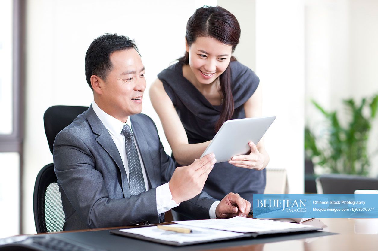 Happy Chinese business colleagues using digital tablet in office