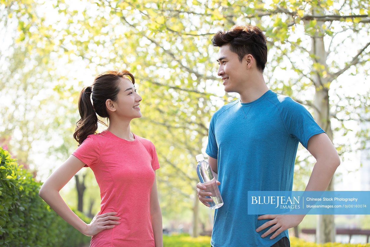 Happy young Chinese couple resting after exercising in park