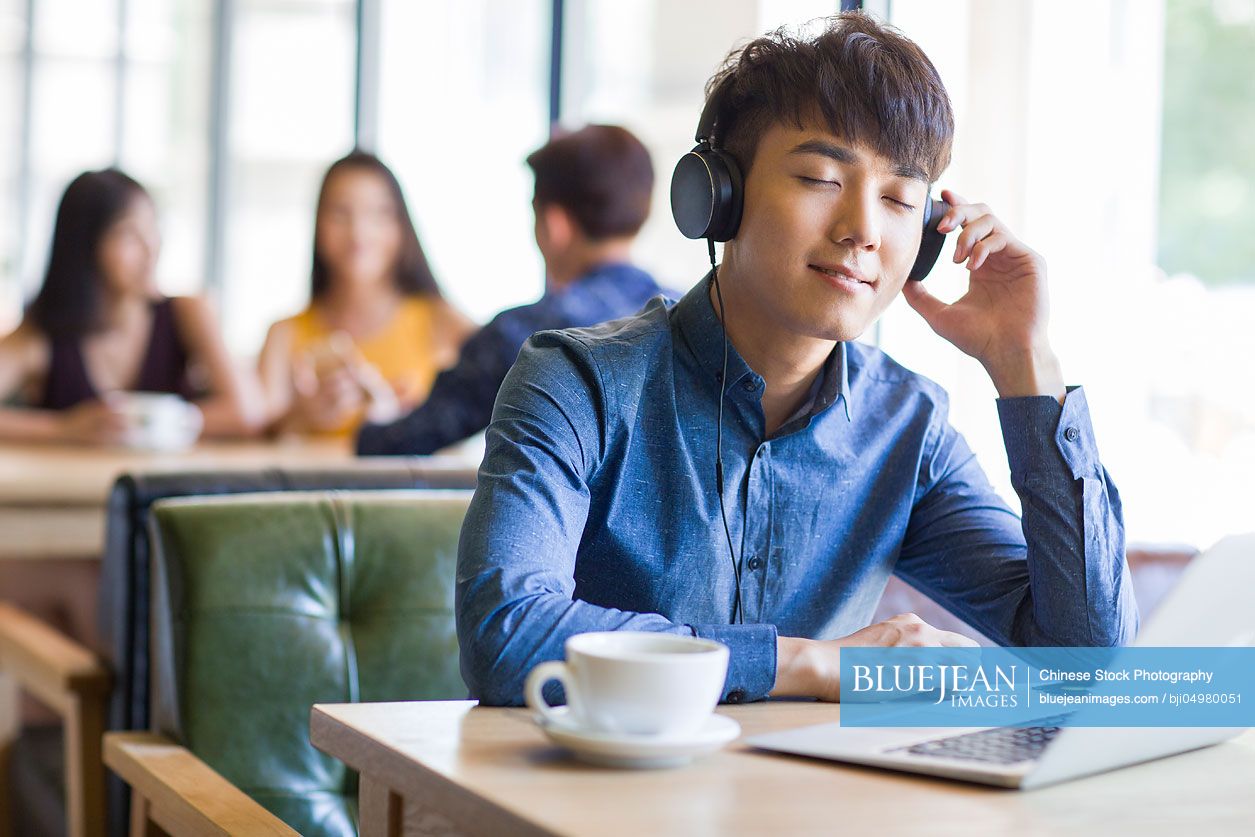 Young Chinese man listening to music in café