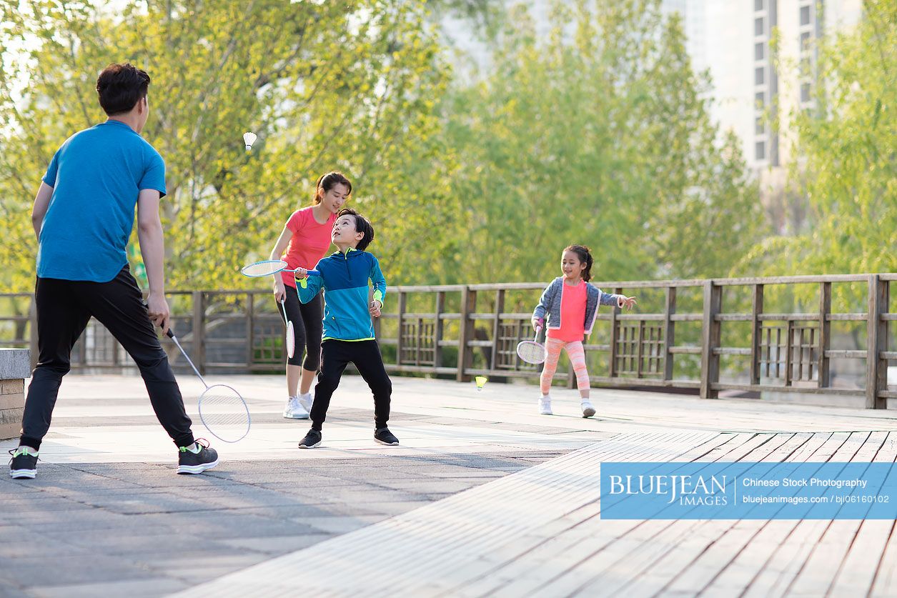 Happy young Chinese family playing badminton in park