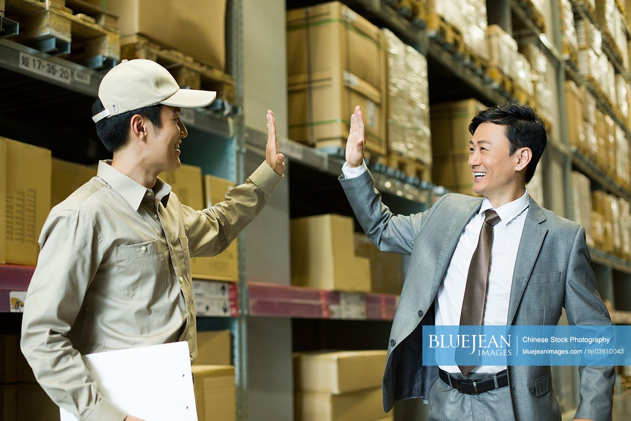 Young Chinese logistics staff doing high five with businessman