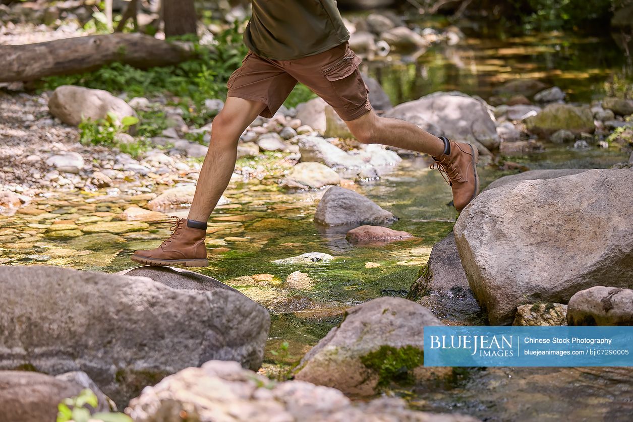 Man crossing a stream, stepping from stone to stone