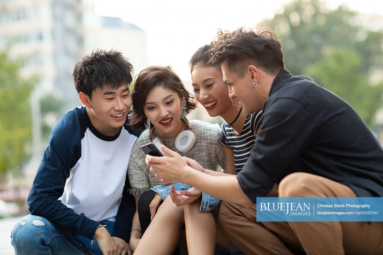 Happy young Chinese friends using smartphone outdoors