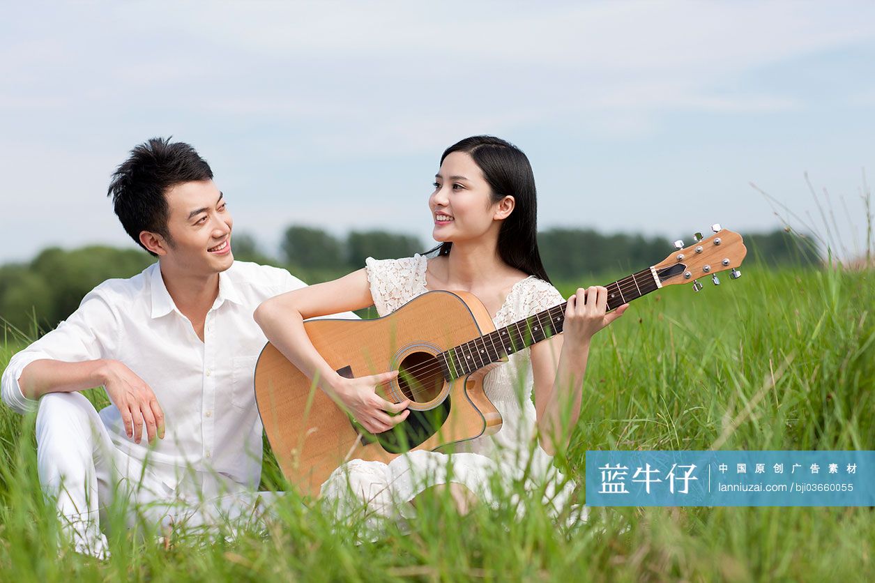 草地上的年轻情侣弹奏吉他