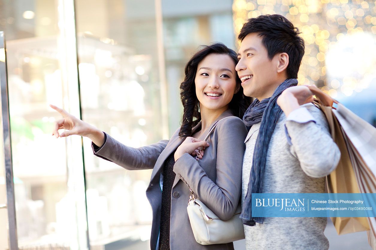 Sweet young Chinese couple doing window-shopping in city street