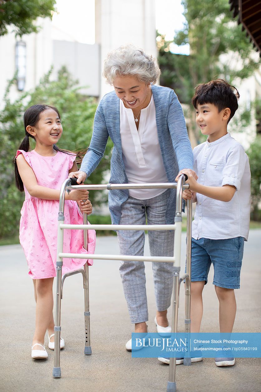 Happy Chinese sibling helping grandma walking with walking frame