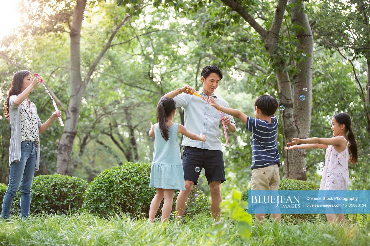 Happy young Chinese family blowing bubbles on grass