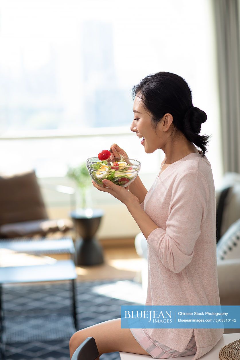 Happy young Chinese woman eating salad at home