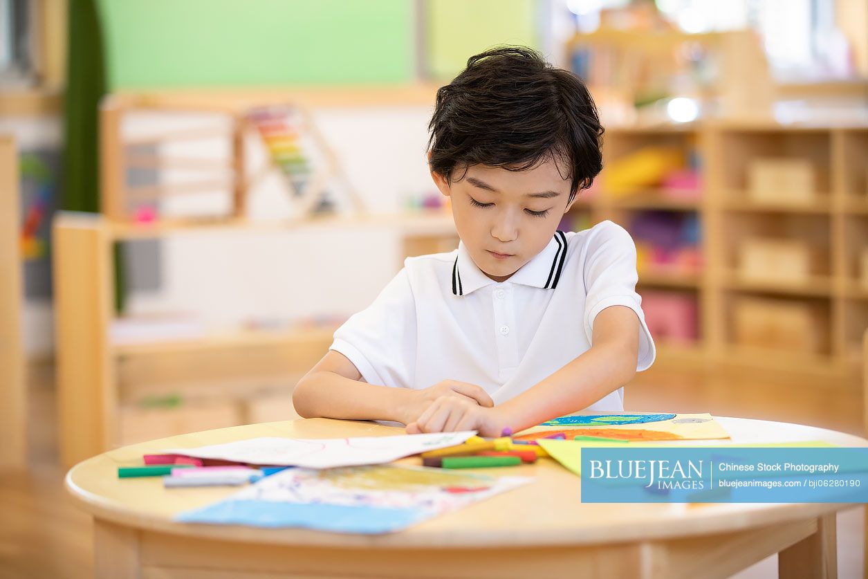 Little Chinese boy painting in classroom