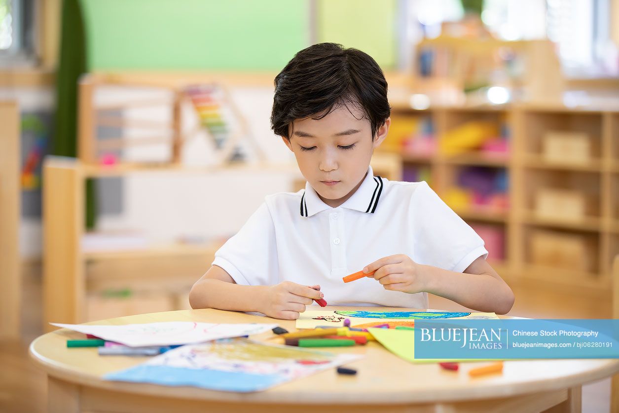 Little Chinese boy painting in classroom