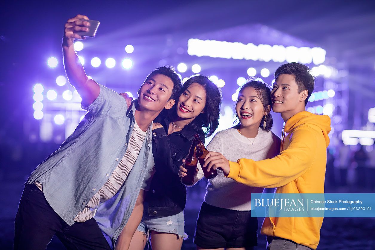 Happy young Chinese friends taking selfie at music festival
