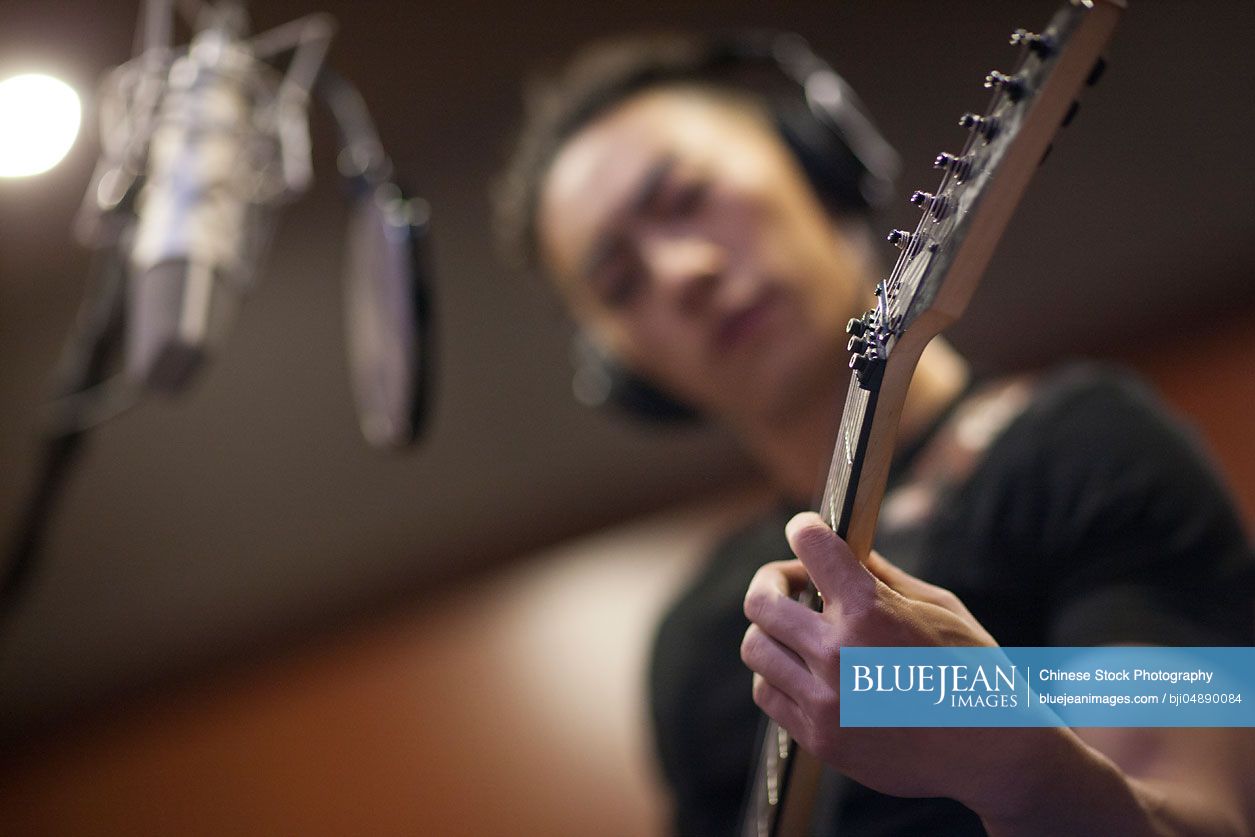Young Chinese man singing with guitar in recording studio