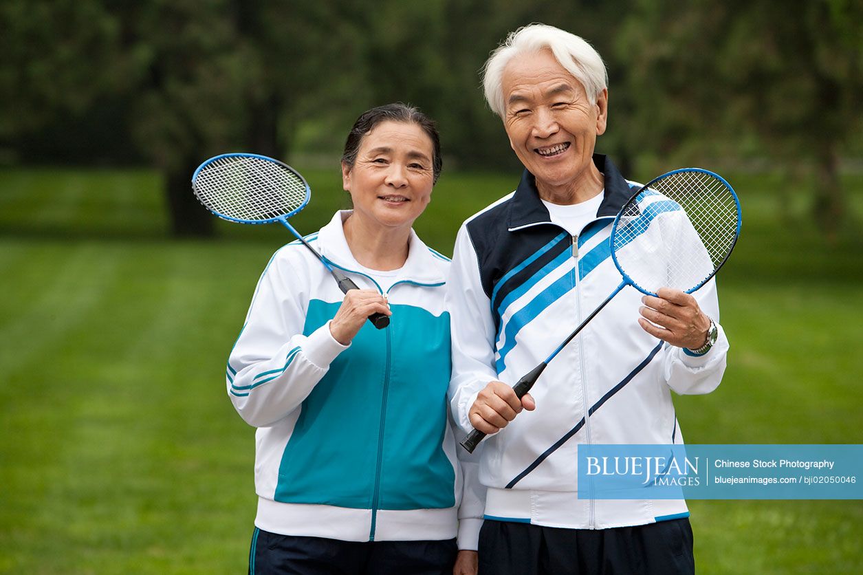 Senior Chinese couple holding badminton rackets in a park