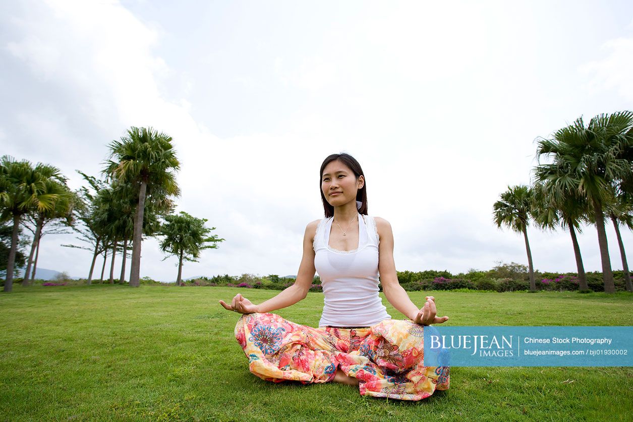 Young Chinese woman doing yoga in grass