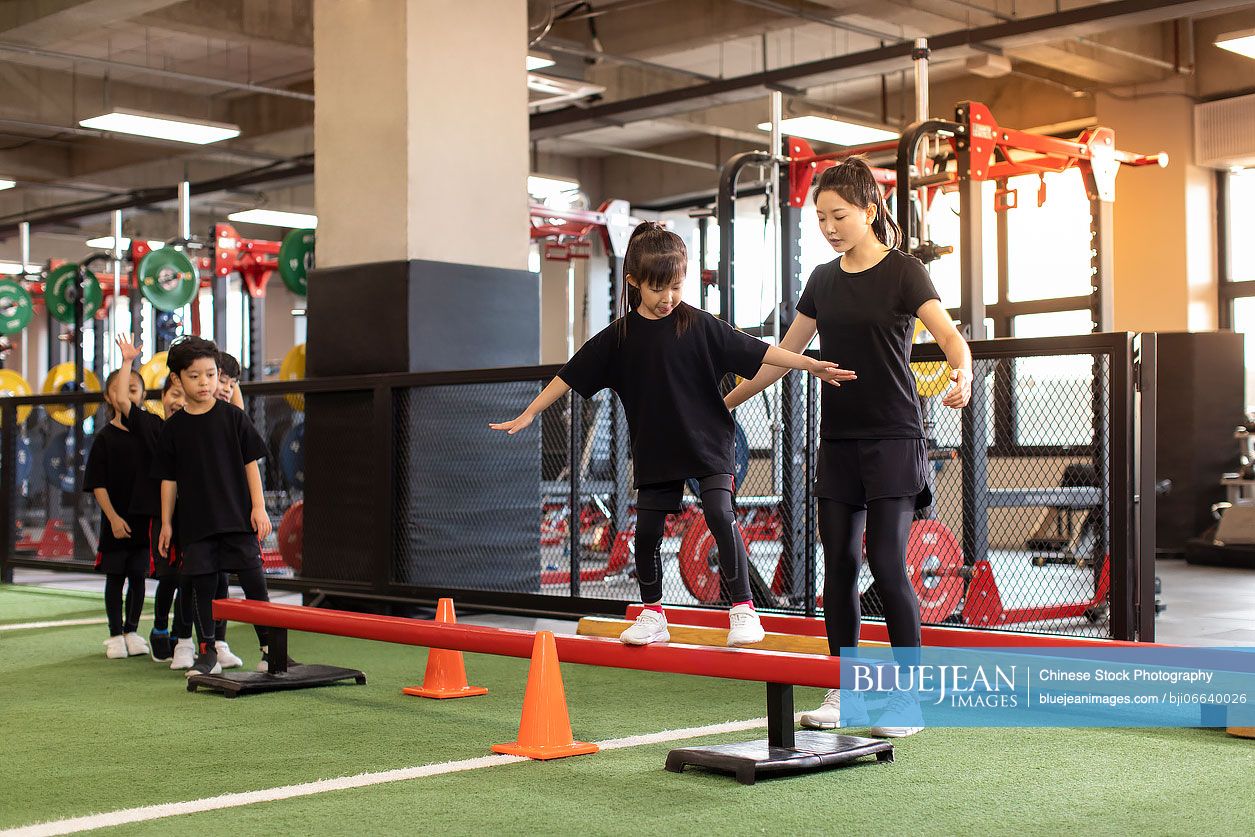 Active Chinese children having exercise class with their coach in gym