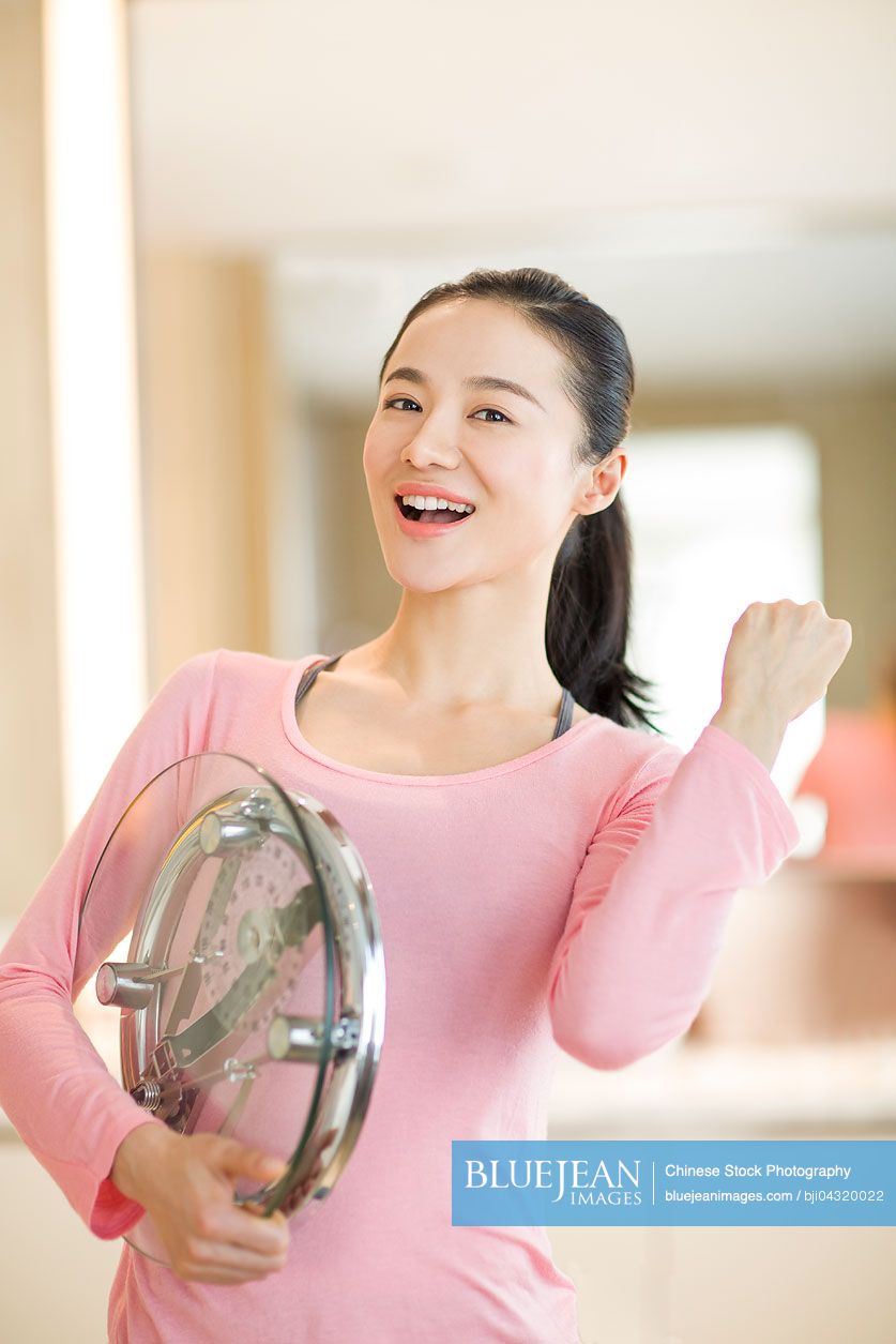 Happy young Chinese woman holding weight scale