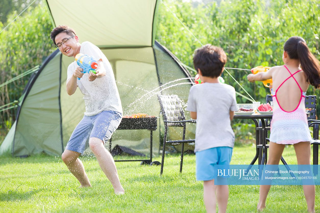 Happy Chinese father and children playing squirt guns