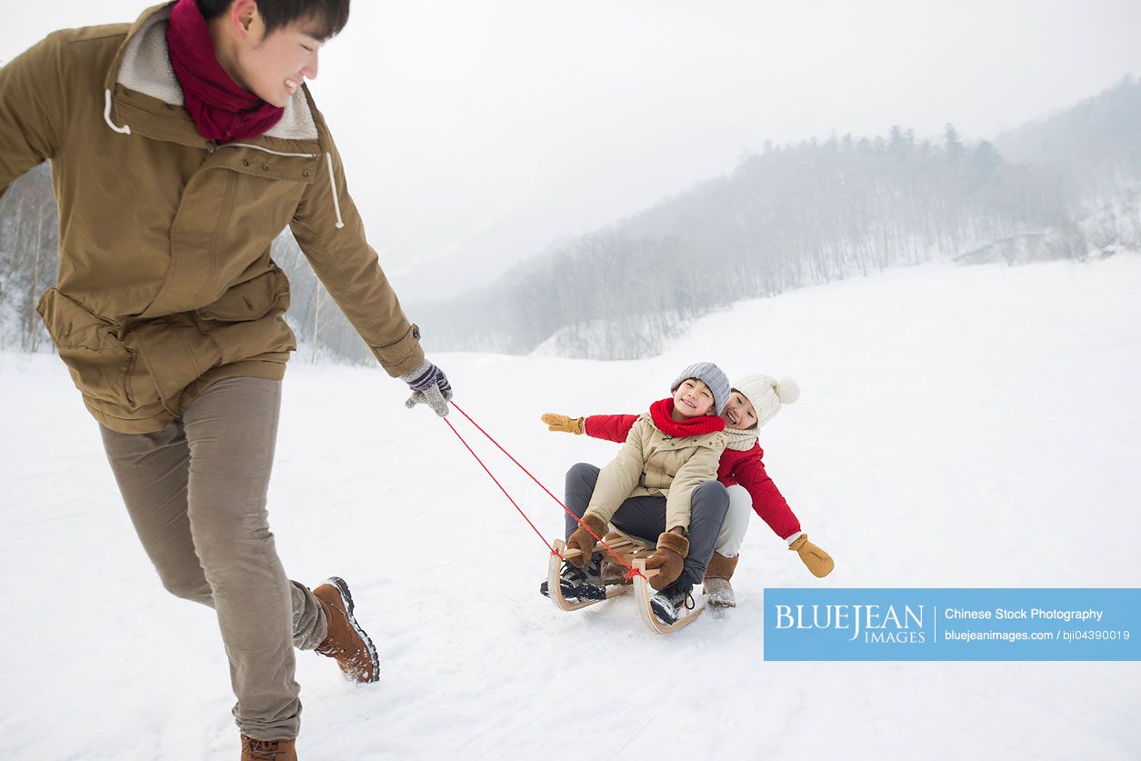 Young Chinese father pulling his children on sled