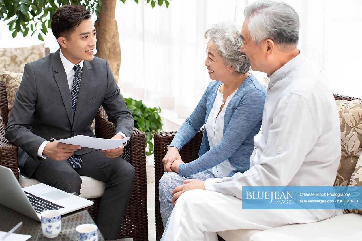 Happy senior Chinese couple talking with financial advisor in living ...