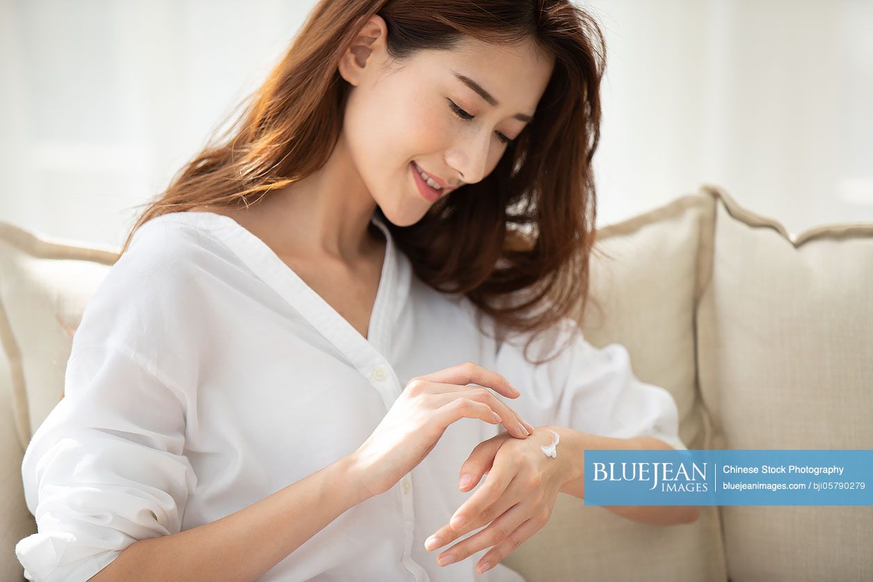 Young Chinese woman applying moisturizer at home
