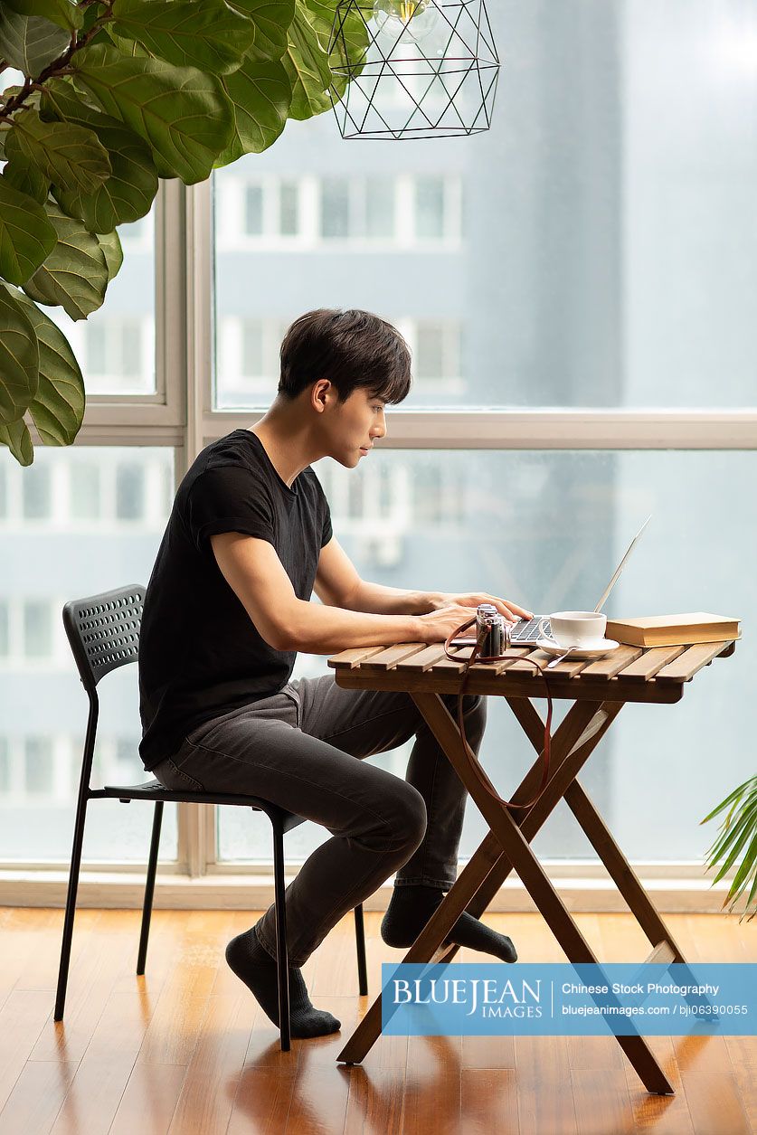 Young Chinese photographer using laptop at home