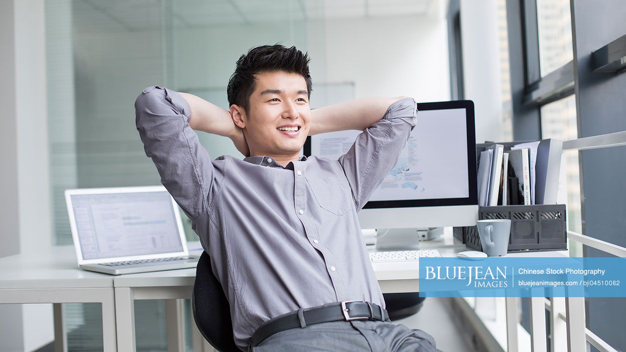 Young Chinese businessman looking through window in office