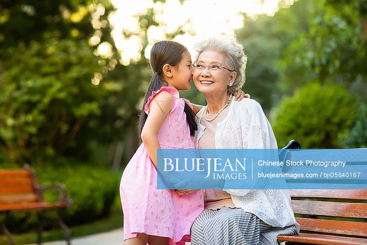 Happy Chinese grandmother and granddaughter whispering in park